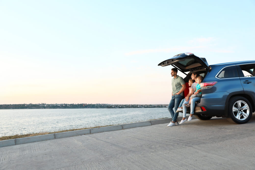 Familia junto a su auto frente al agua, reflejando beneficios de seguros de autos para hispanos en EE. UU.