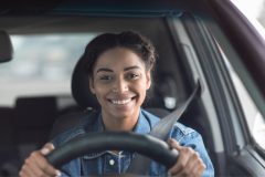Mujer hispana conduciendo y sonriendo.