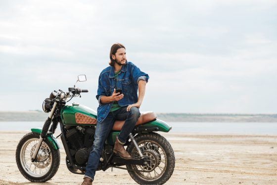 Hombre a un costado de la playa sentado en su motocicleta.