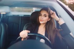 Mujer hispana sonriendo en su auto mientra maneja.