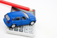 Carro de juguete simbólico a un seguro de auto encima de una calculadora.