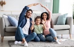 Familia hispana joven formando una casa con sus manos y sonriendo por tener un seguro de hogar barato