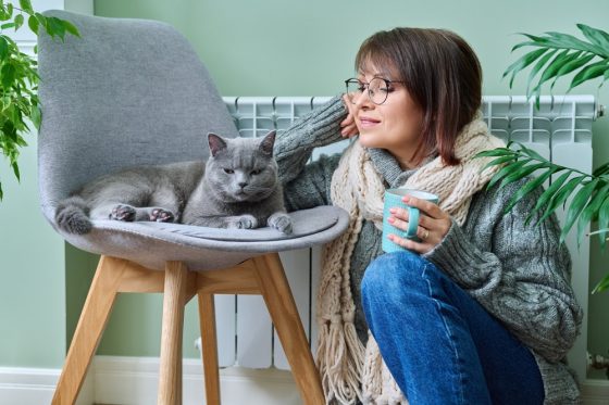 Mujer y gato tratando de mantenerse calientes y lograr un ahorro de energía