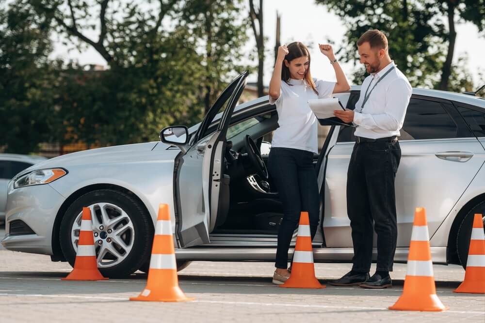 Mujer celebrando junto a su auto después de aprobar el examen de manejo DMV en California.