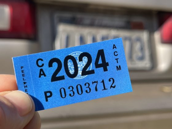 Hombre sujeta su nueva etiqueta tras renovar sticker de carro en California