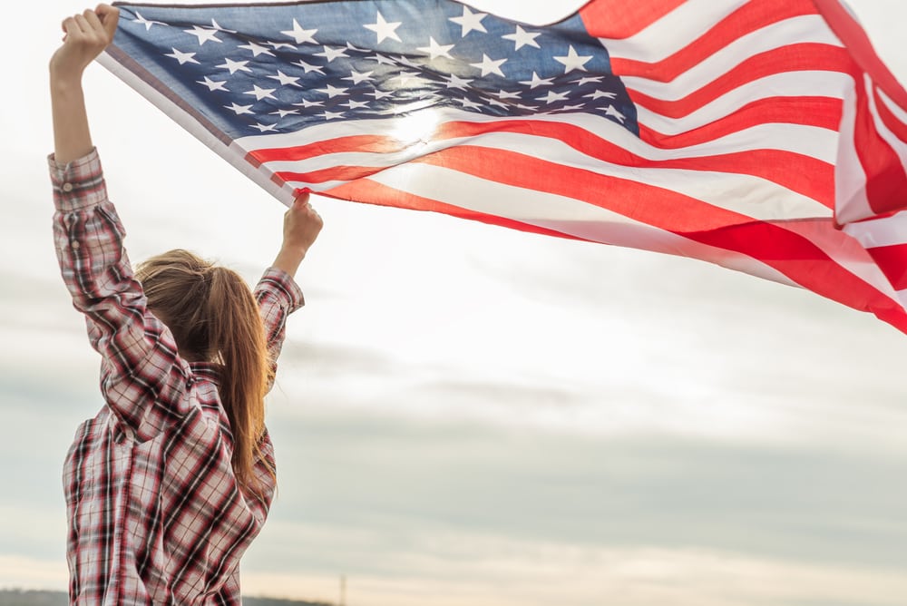 Mujer ondeando la bandera de USA después de solicitar uno de los tipos de visas para ingresar a los Estados Unidos