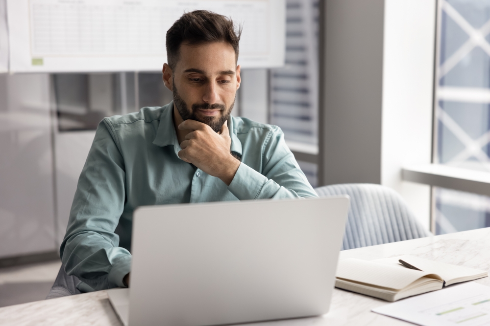Hombre revisando una laptop con expresión pensativa, representando el proceso de solicitud y seguimiento de un permiso de trabajo.