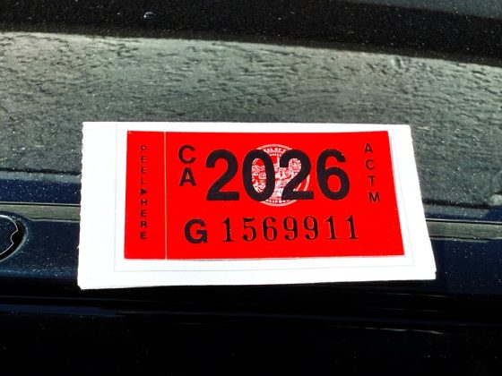 Primer plano de etiqueta roja 2026 en el parabrisas de un auto, representando la registración en California vigente.