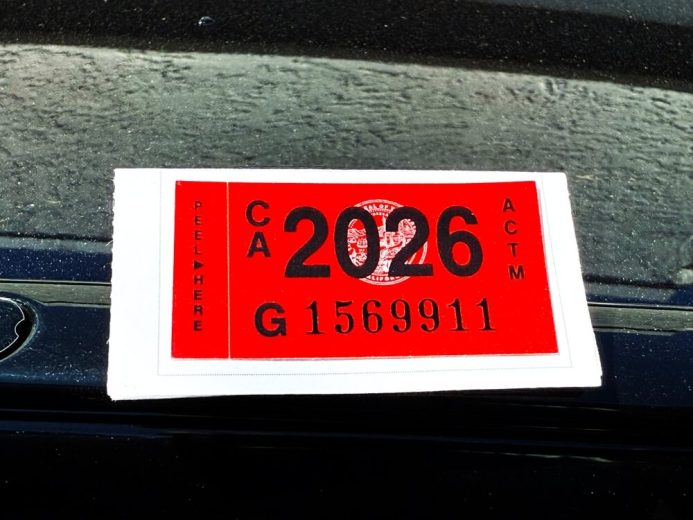 Primer plano de etiqueta roja 2026 en el parabrisas de un auto, representando la registración en California vigente.