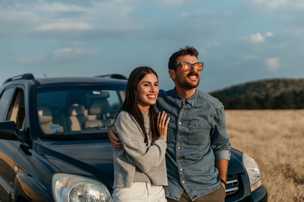 Pareja sonriendo junto a su auto durante un viaje, representando cómo pagar la placa del carro en línea en California.