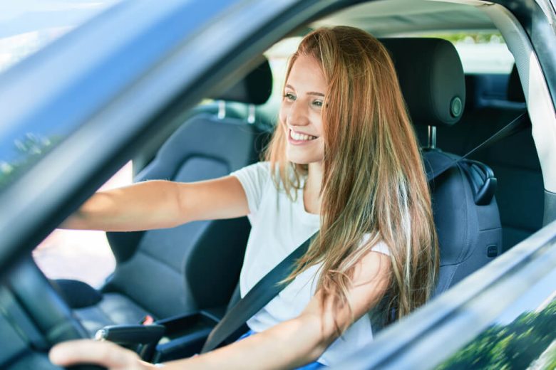Mujer universitaria conduciendo un vehículo - Cómo elegir el mejor seguro de auto si eres estudiante en California - Cost-U-Less
