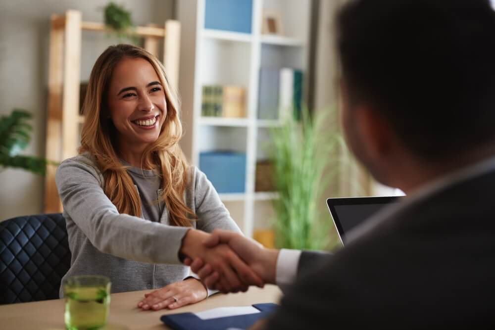 Mujer joven estrechando la mano de un asesor durante una reunión, representando la contratación de un seguro de vida para persona sin dependientes.