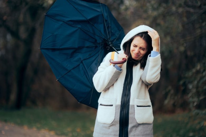 Persona luchando contra el viento y la lluvia con un paraguas, reflejando el impacto personal de las tormentas en California