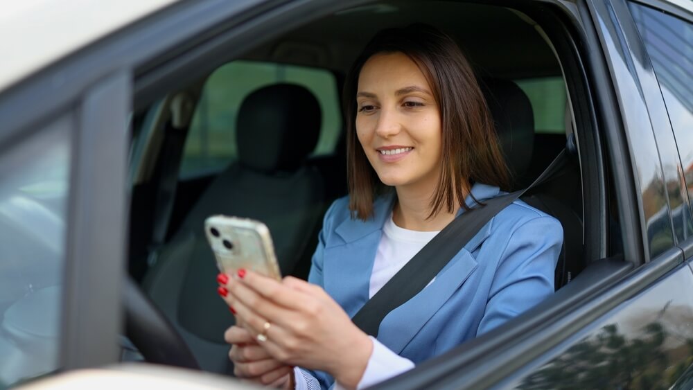 Mujer dentro de su auto revisando su teléfono tras recibir aviso de que la aseguradora no renueva tu póliza de auto en California.