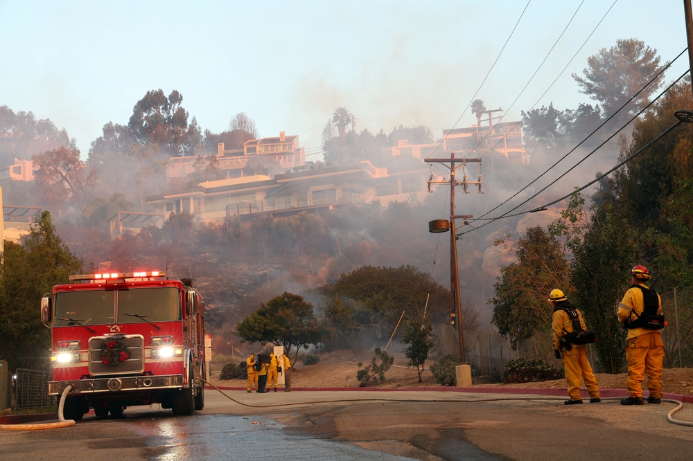 Camión de bomberos y equipos combatiendo incendio en zona residencial, reflejando zonas de riesgo en California
