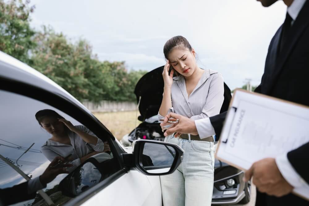 Conductora con auto descompuesto hablando con agente, ilustrando la importancia del seguro de auto y vehículo en proceso de venta ante imprevistos.