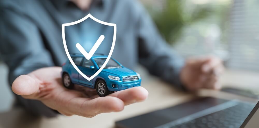 Mano sosteniendo un auto con ícono de protección, simbolizando el seguro de auto y vehículo en proceso de venta y su cobertura.