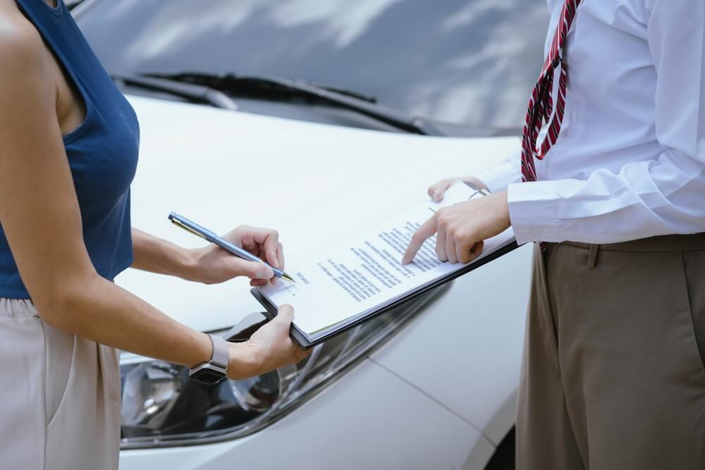 Conductora firmando documentos junto a un agente frente a un automóvil, representando el proceso de obtener seguro de auto con licencia suspendida.