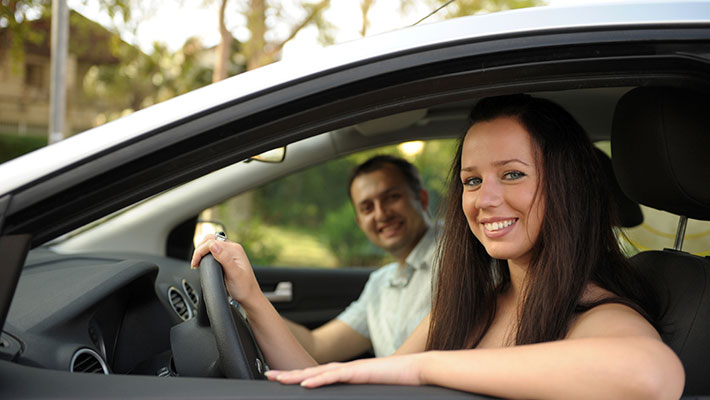 Una joven sonriente conduciendo un automóvil asegurado