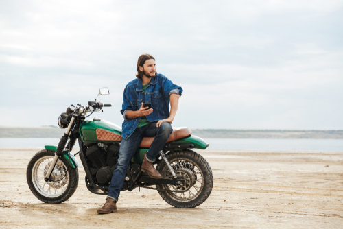 Hombre a un costado de la playa sentado en su motocicleta