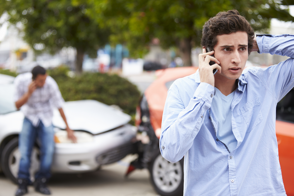 Hombre joven llamando por teléfono después de un accidente en el que los conductores tienen seguros para autos en California 