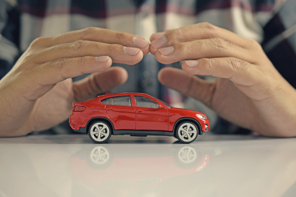 Hombre cubriendo con sus manos un auto de juguete simbolizando una cobertura de seguro de auto