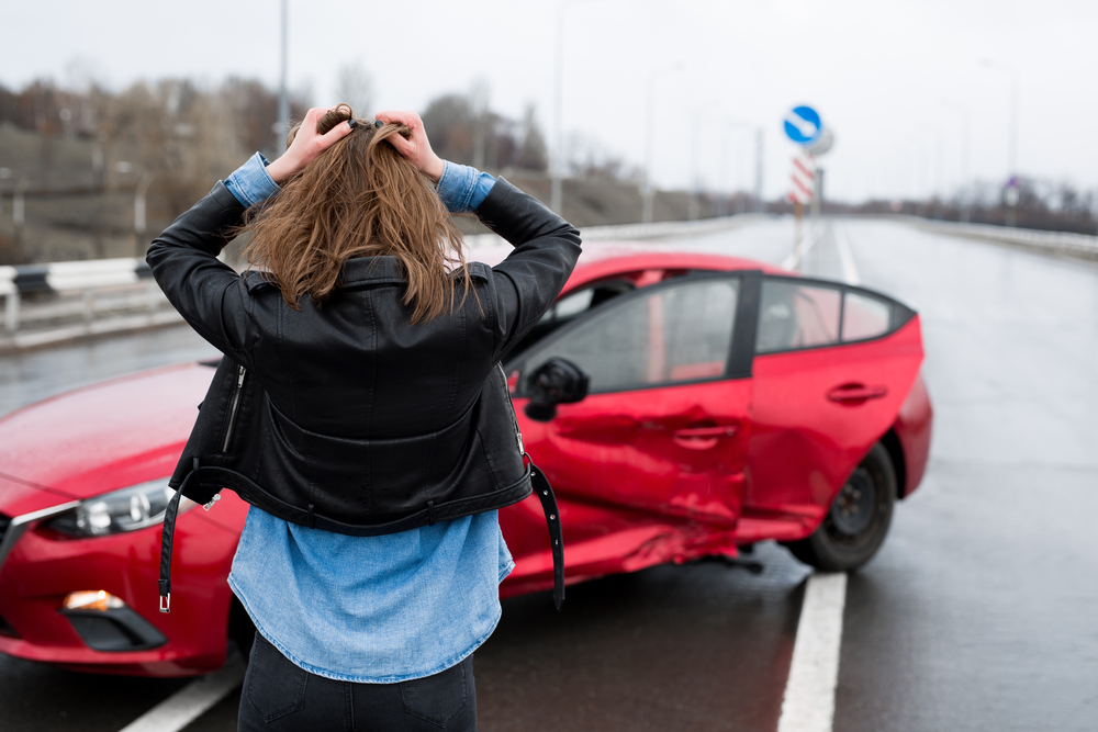 Mujer viendo su auto perjudicado por un accidente auto y preocupada por tener la aseguranza de carro en California correcta