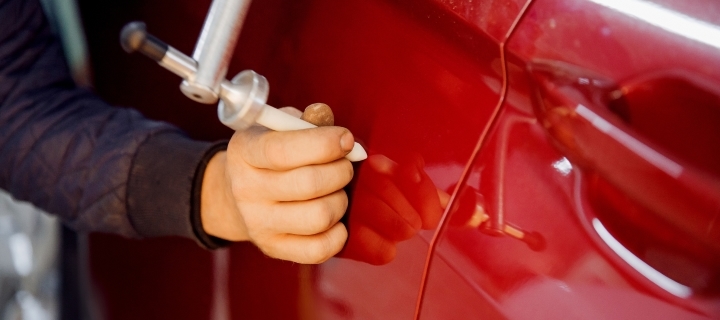 Persona usando una pluma de pintura para reparar una abolladura en auto