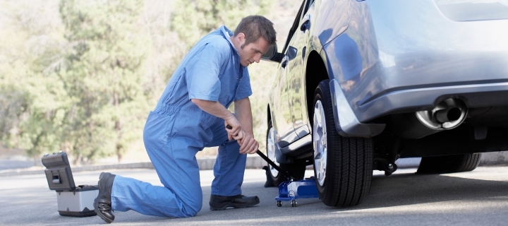 Hombre reparando llanta ponchada de auto gris