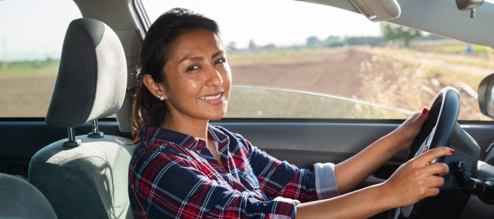 Mujer latina sonriendo al conducir por tener un buen seguro de auto barato.