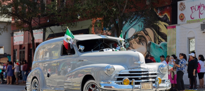 Vehículo blanco con banderas mexicanas en un desfile, protegido con seguro de auto clásico.