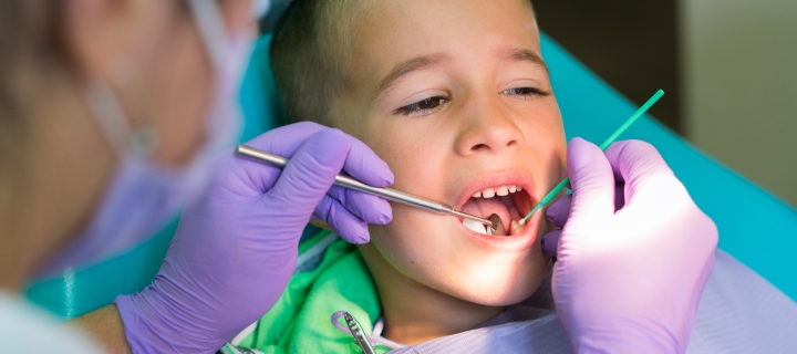 Niño hispano abriendo la boca para ser revisado por mujer dentista.