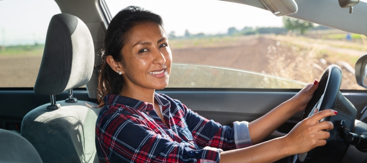 Mujer latina sonriendo al conducir por tener un buen seguro de auto barato