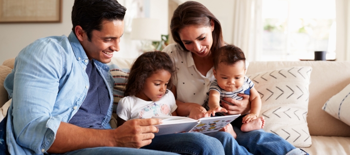 Familia latina en la sala de su casa leyendo un cuento.