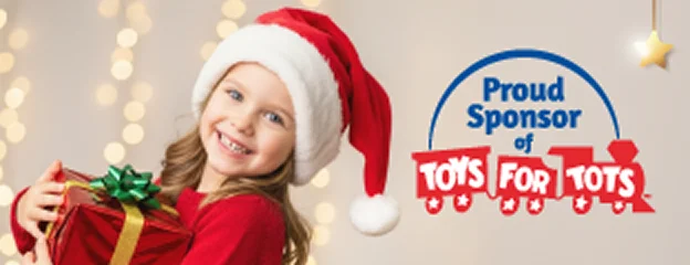 Una niña sonriente con un gorro de Santa y un suéter rojo sostiene un regalo envuelto frente a luces navideñas, junto al texto que dice “Orgulloso patrocinador de Toys for Tots”.